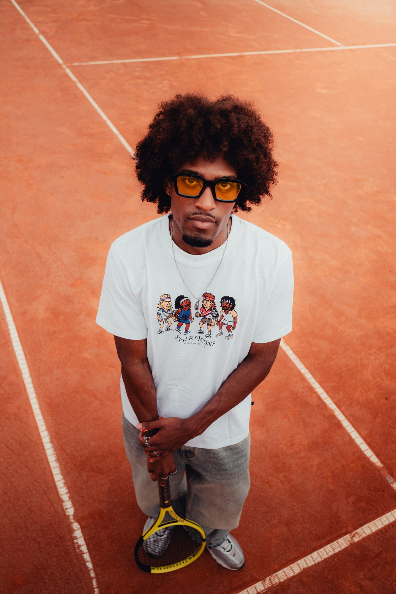 COLORBLND Model mit Afro und gelber Sonnenbrille auf rotem Tennisplatz