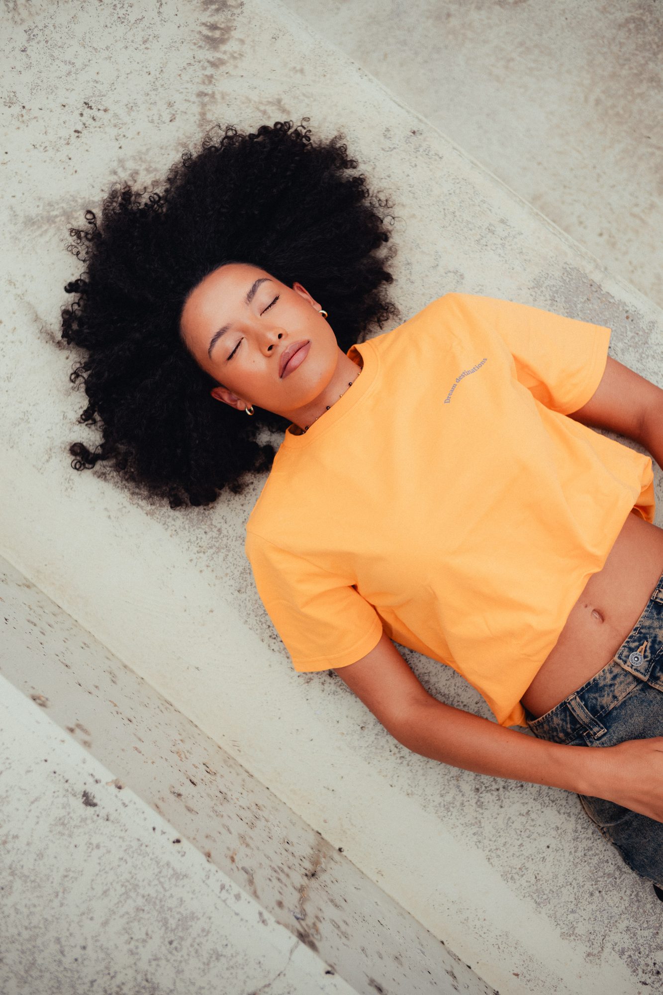 COLORBLND Model in orangem Crop-Top liegend auf Betonuntergrund